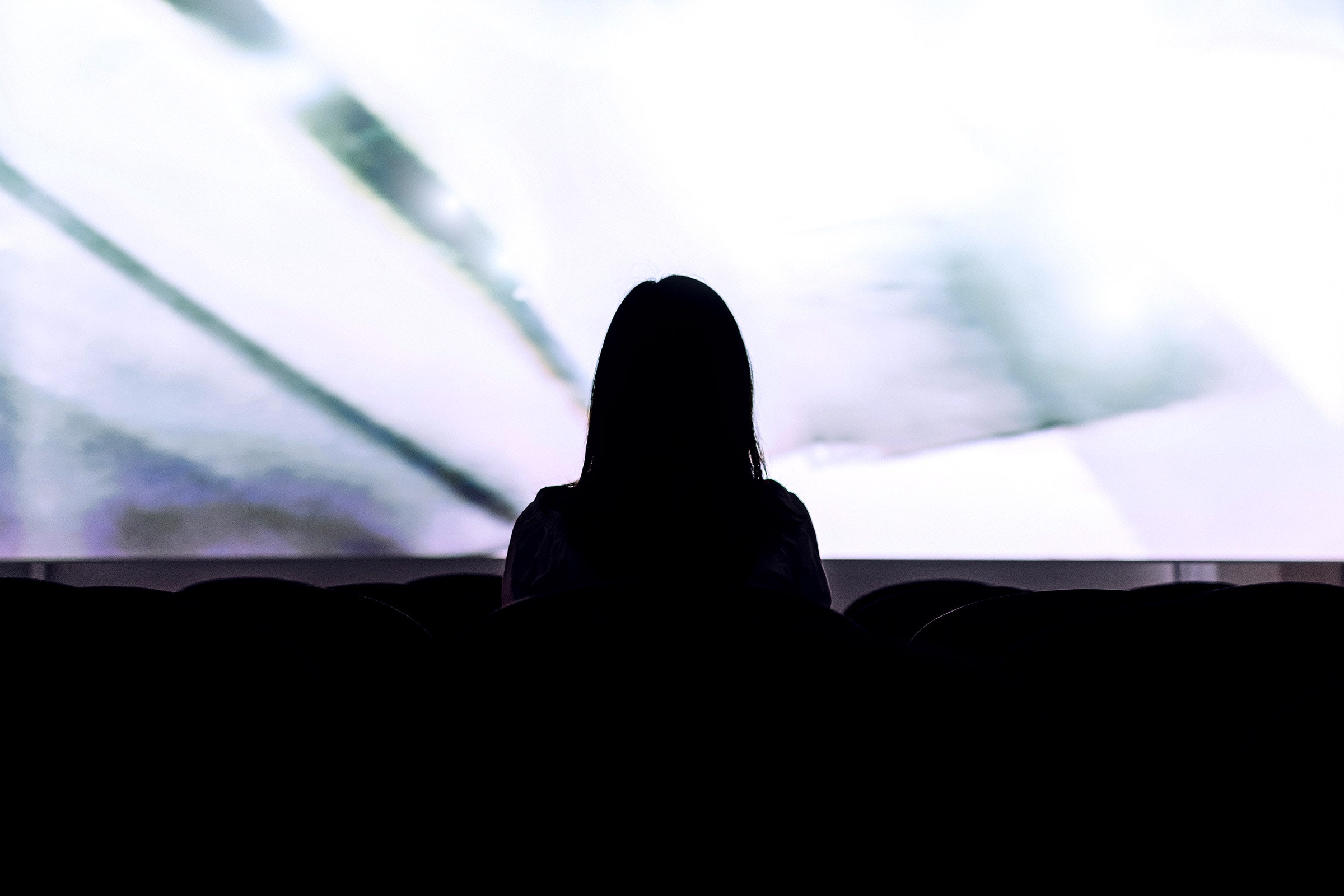 Silhouette of a person sitting in front of a large screen in a movie theater